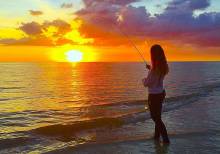 Woman fishing on the beach at sunset