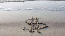 Dollar sign drawn into the beach sand with small wave
